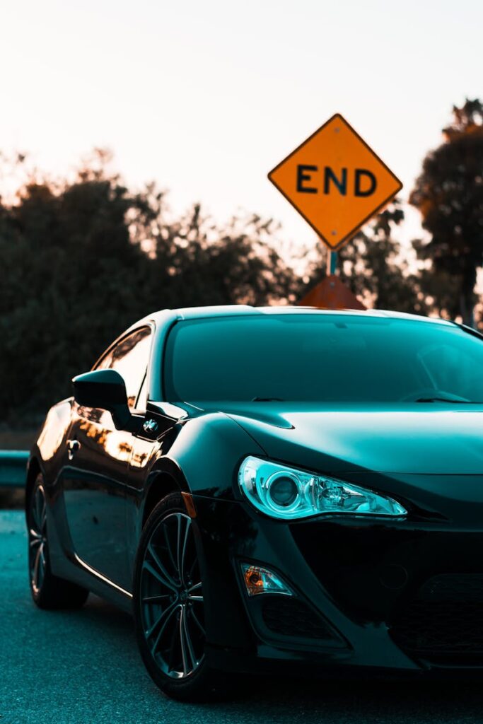 Stylish black luxury car parked near a road end sign, surrounded by lush greenery.